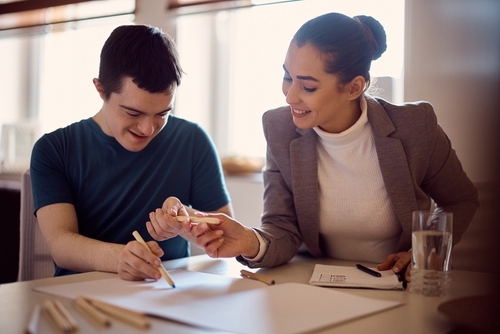 happy down syndrome man and his psychologist drawing together on the paper during home visit