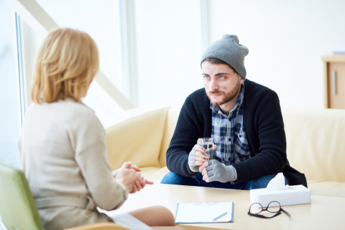 young migrant or victim of terrorism with glass of water listening to advice of social worker in center of support