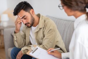 A man appears distressed, with one palm covering his face, during a psychological counseling session