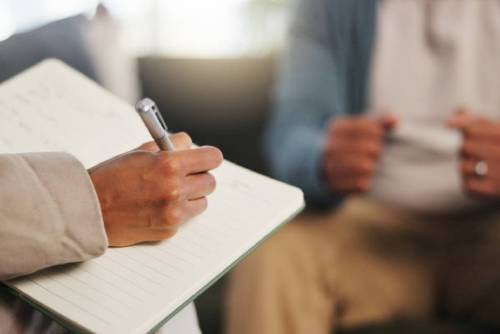 Book, therapy and hand of therapist writing notes for client with mental health evaluation