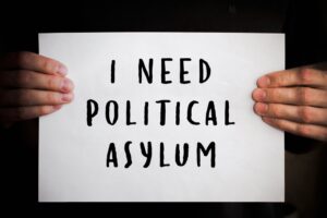 male hands holding white sheet of paper with text I need political asylum