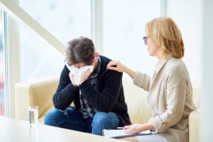 Psychologist giving advice to her addicted patient crying in handkerchief while sharing his troubles during session
