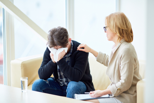 Psychologist giving advice to her addicted patient crying in handkerchief while sharing his troubles during session