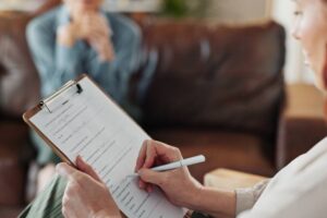 Psychologist, clipboard and hands of woman with notes and office from mental health assessment in consultation