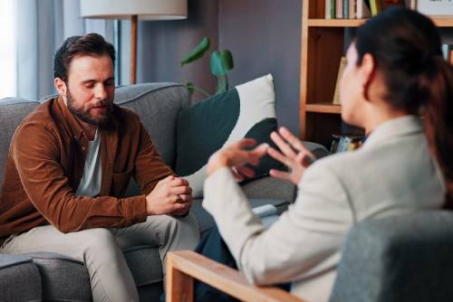 Psychologist and patient talk in therapy session. Clinician writes notes on a clipboard as a man talks about mental health during consultation. (2)